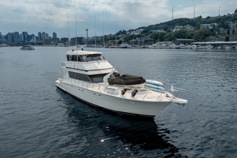 Slide: The Image of 1988 Hatteras 65 Sportfish yacht cruising in a scenic harbor with city skyline backdrop. - 2
