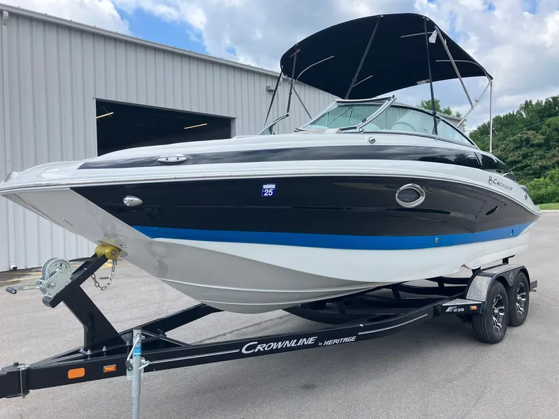 The Image of 2023 Crownline Eclipse E235 boat on trailer, parked near a building under a cloudy sky. - 0