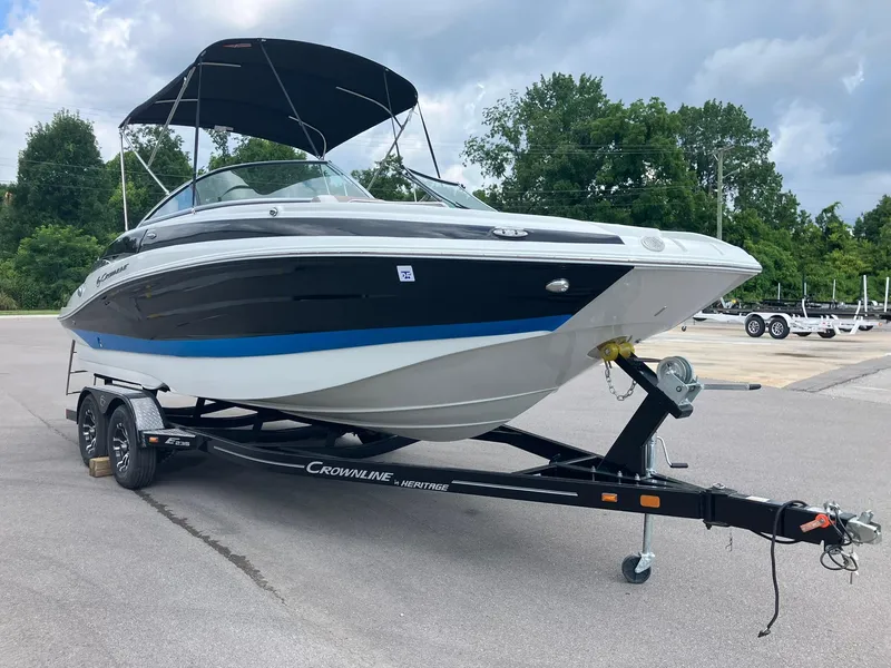 Slide: The Image of 2023 Crownline Eclipse E235 boat on trailer, parked outdoors with trees in background. - 1