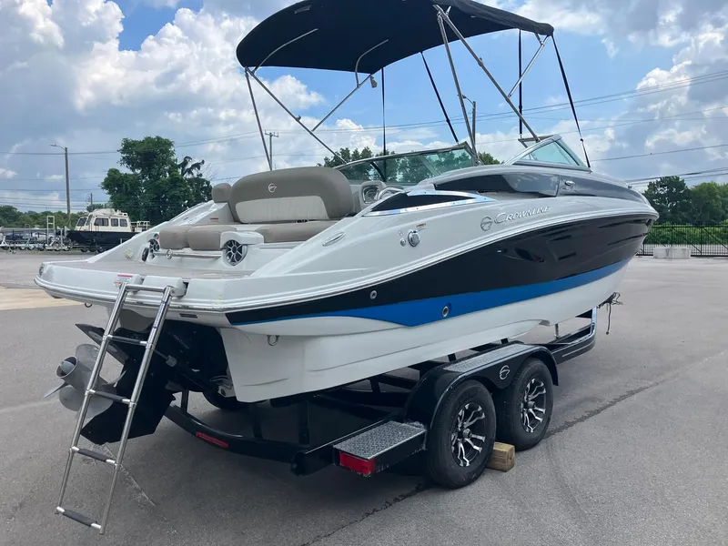 Slide: The Image of 2023 Crownline Eclipse E235 boat on trailer, featuring sleek design and canopy under cloudy sky. - 2