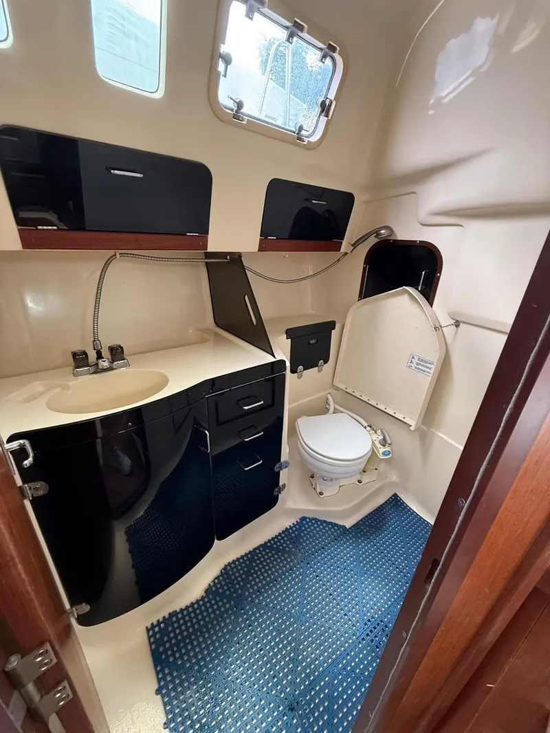 Slide: The Image of 1995 Hunter 336 yacht bathroom with sink, toilet, storage cabinets, and blue mat. - 4