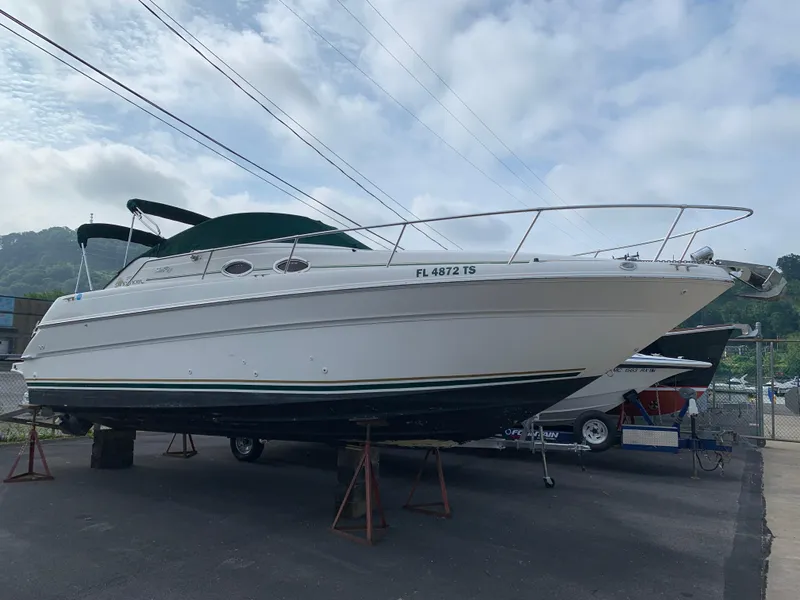 Slide: The Image of 2000 Sea Ray 270 Sundancer boat on stands, parked outdoors under cloudy sky. - 23
