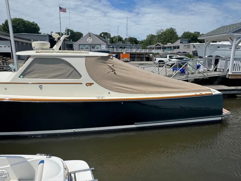 Slide: The Image of 1999 Hinckley Picnic boat docked with cover, marina background, American flag visible. - 3