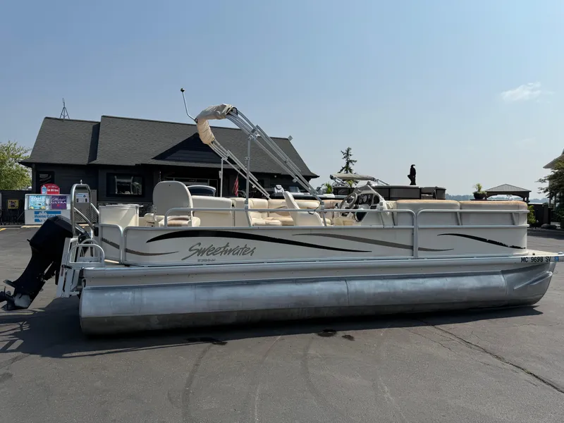 Slide: The Image of 2006 Sweetwater 23860DF pontoon boat parked on pavement near a building. - 3