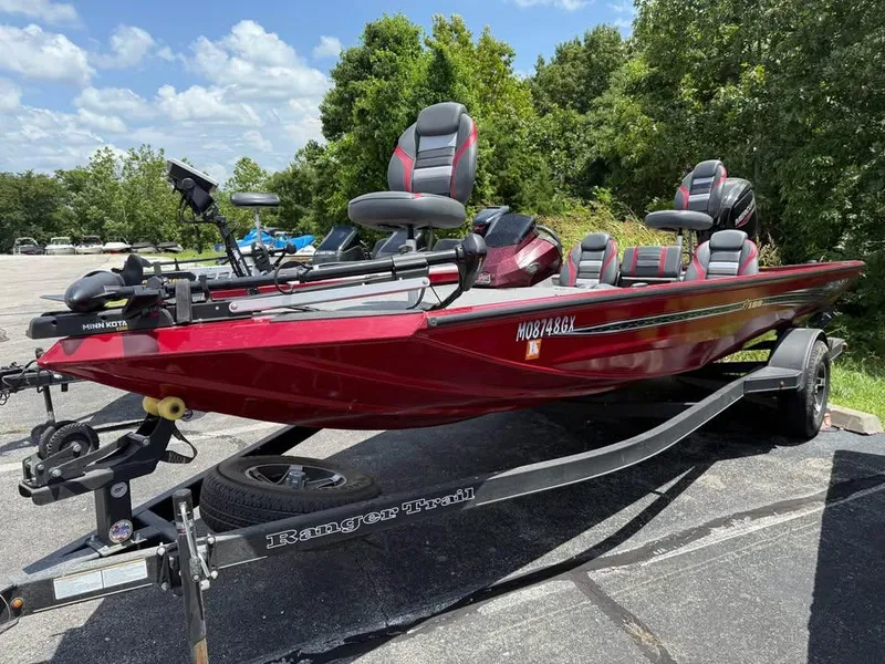 Slide: The Image of 2023 Ranger RT 188 boat in red, parked on a trailer, surrounded by trees. - 2