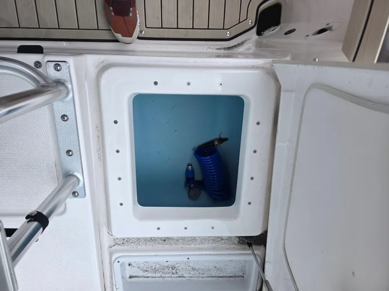 Slide: The Image of Open storage compartment on 2025 Yamaha Boats 195 FSH Sport, featuring a blue hose inside. - 8