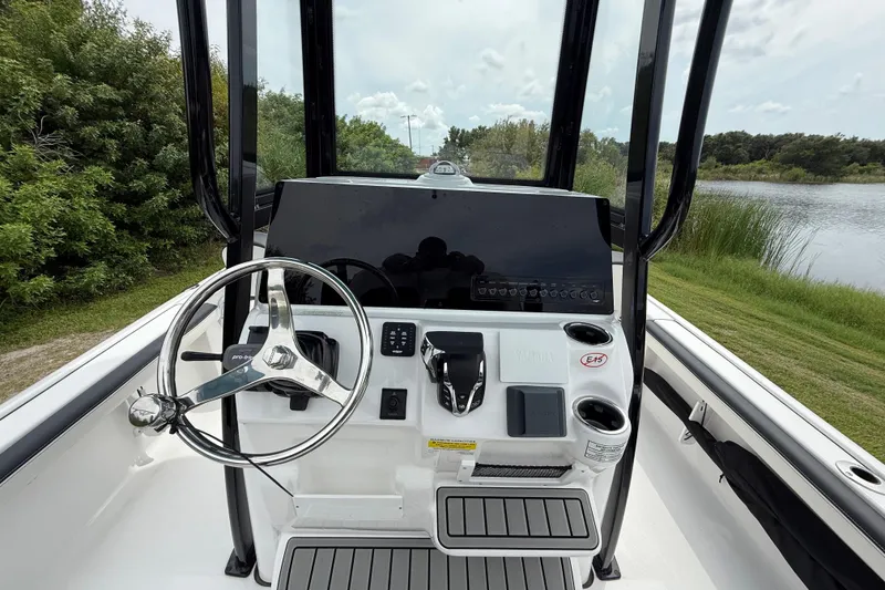 Slide: The Image of 2026 Tidewater 2300 Carolina Bay boat console with steering wheel and controls, near a serene lake. - 14