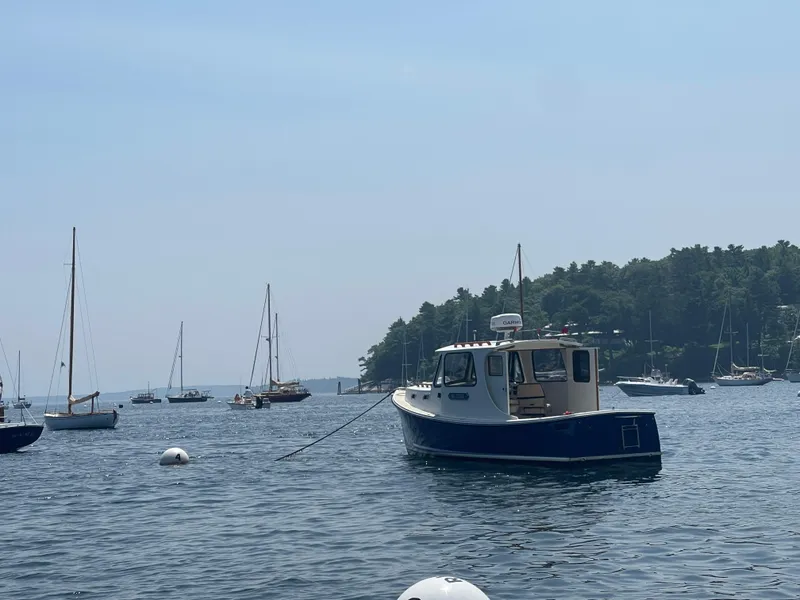 Slide: The Image of 2005 Atlas Boat Works Pompano 21 on calm water with sailboats and forested shoreline. - 20