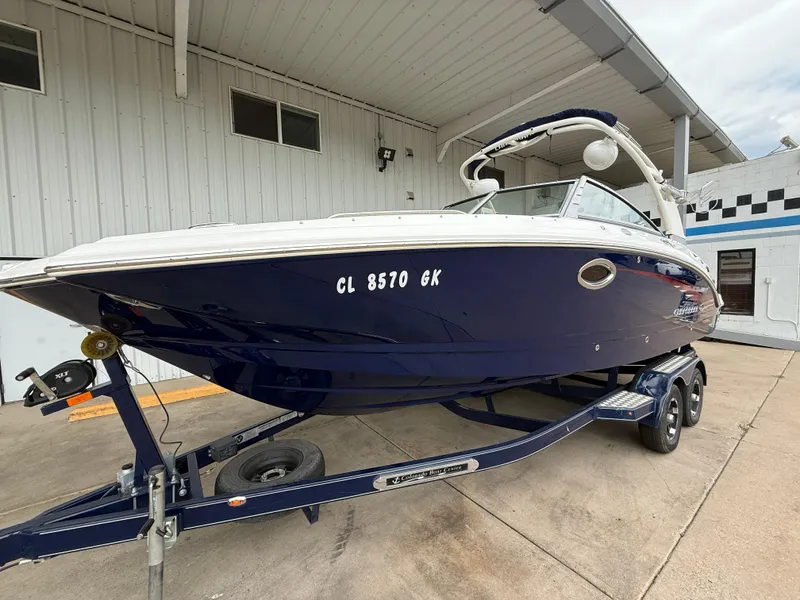 Slide: The Image of 2018 Chaparral 244 Sunesta Surf boat on trailer, parked under a metal roof. - 2