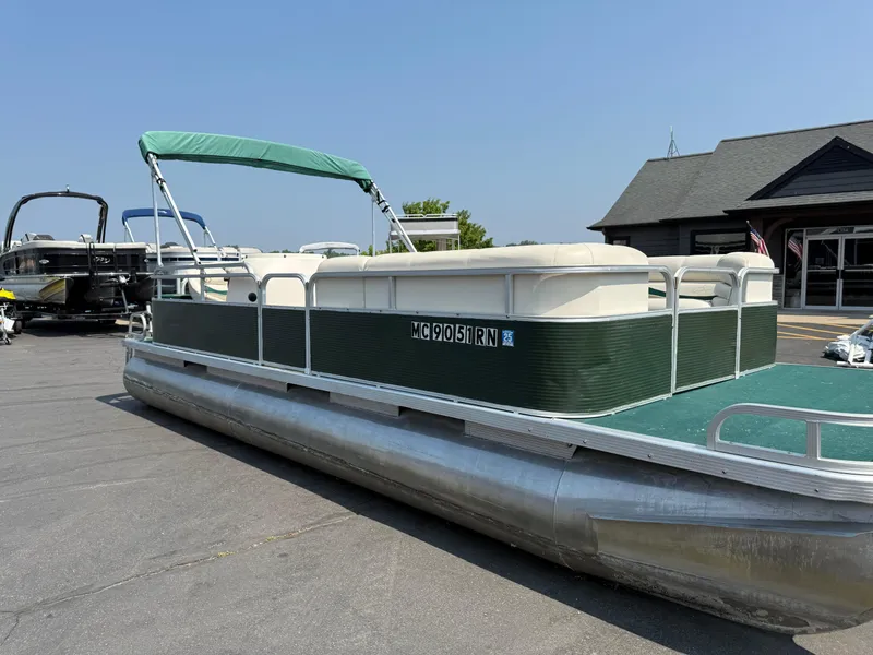 Slide: The Image of 1998 Bennington 22 pontoon boat with green canopy, parked on pavement near a building. - 2