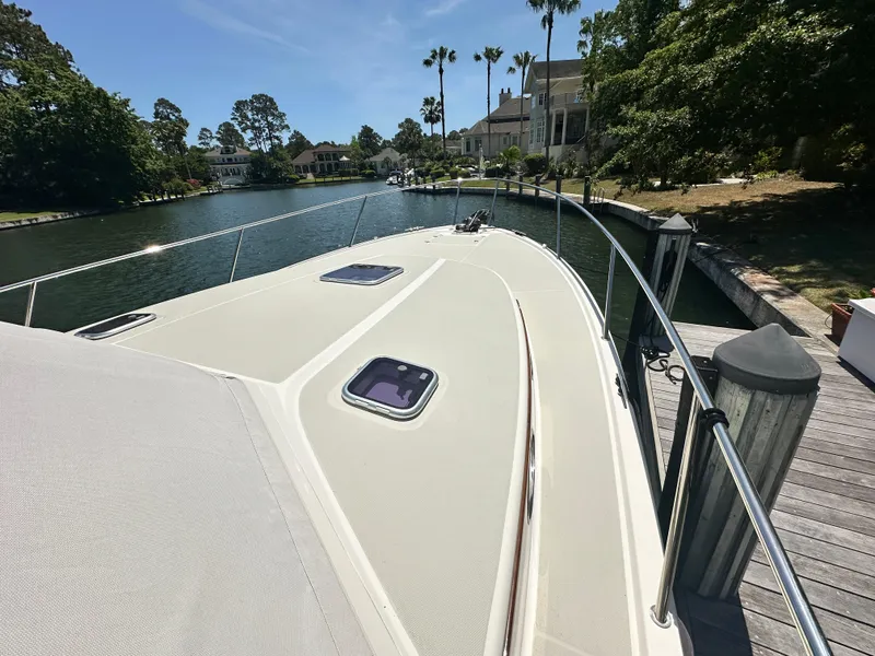 Slide: The Image of 2022 Back Cove 372 yacht docked by a scenic waterfront with lush greenery. - 11