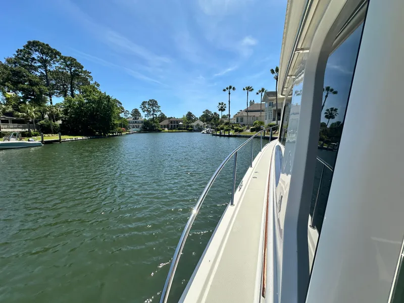 Slide: The Image of 2022 Back Cove 372 yacht cruising on a scenic, tree-lined waterway under a clear blue sky. - 40