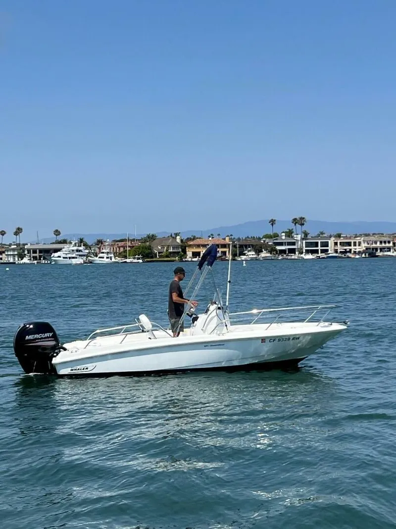 Slide: The Image of 2016 Boston Whaler 180 Dauntless boat on water, person standing, coastal background. - 9