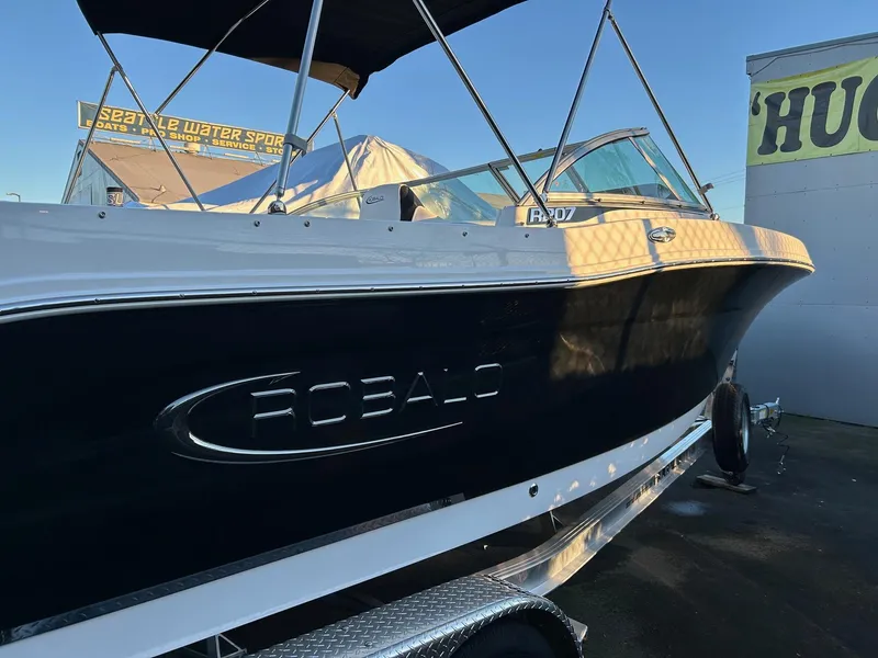 Slide: The Image of 2026 Robalo R207 Dual Console boat on trailer, side view, under clear blue sky. - 32