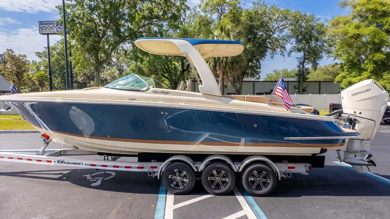 Slide: The Image of 2025 Chris-Craft Launch 28 GT boat on trailer, blue and beige design, parked outdoors. - 4
