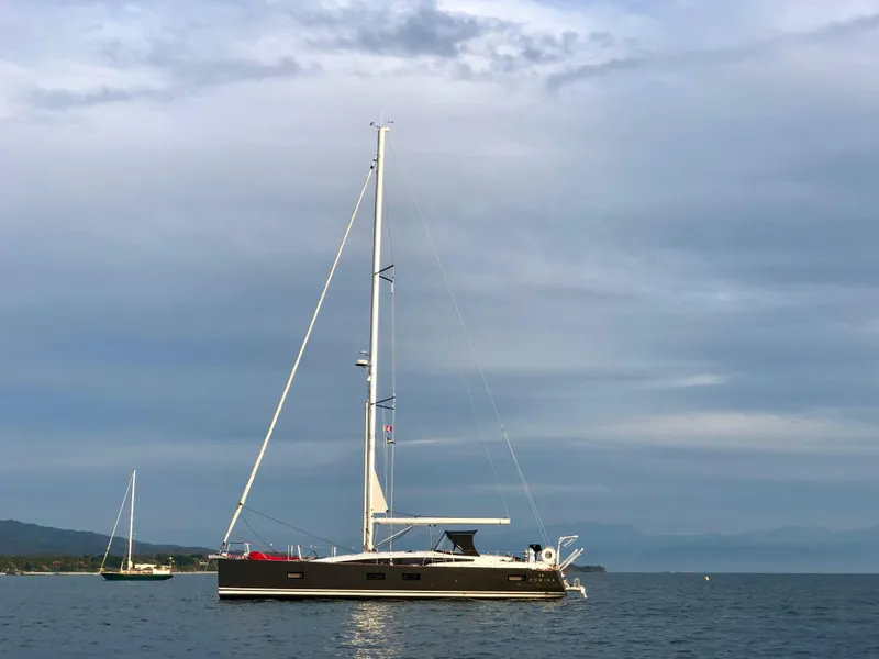 Slide: The Image of 2018 Jeanneau 54 sailboat anchored on calm water under a cloudy sky. - 7
