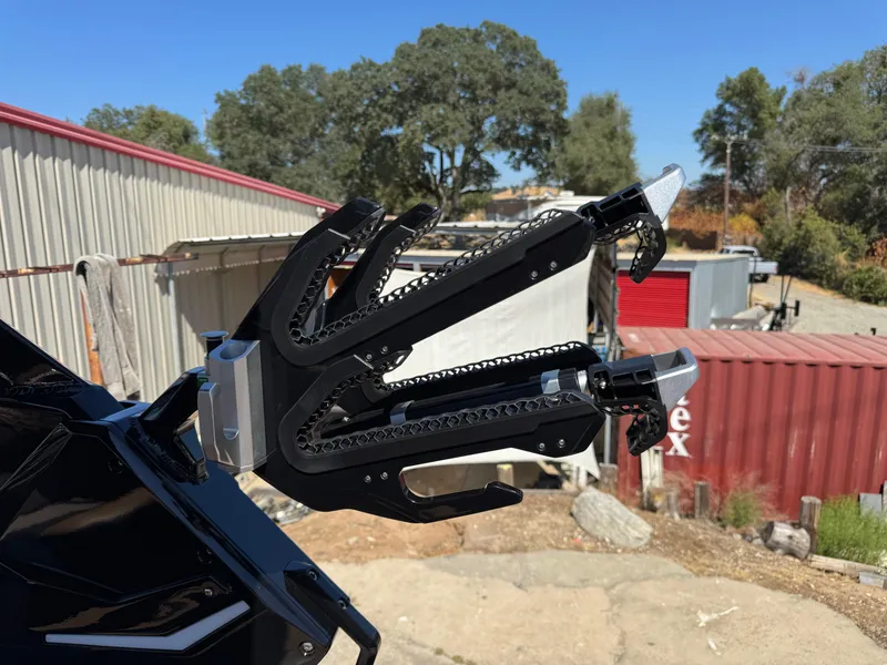 Slide: The Image of Wakeboard rack on 2025 Centurion RI 245 boat, outdoors with trees and containers in background. - 13