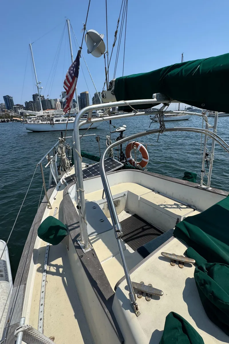 Slide: The Image of 1985 Bluewater Ingrid 38 sailboat docked, featuring green covers and American flag, city skyline in background. - 13