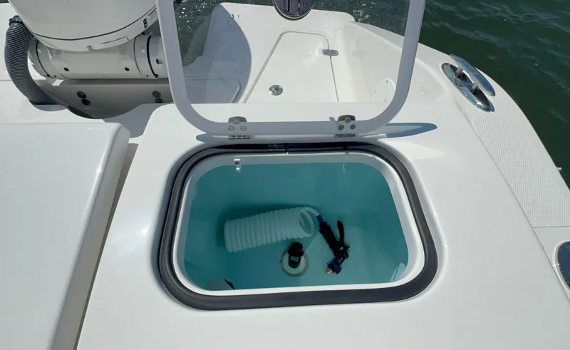 Slide: The Image of Open storage compartment on 2023 Pursuit DC 246 Dual Console boat, featuring coiled hose. - 11