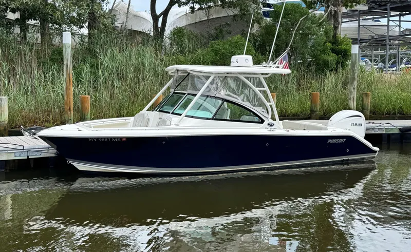 Slide: The Image of 2023 Pursuit DC 246 Dual Console boat docked by lush greenery. - 2