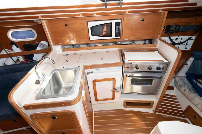 Slide: The Image of 2003 Catalina 310 yacht kitchen with sink, stove, microwave, and wooden cabinetry. - 13