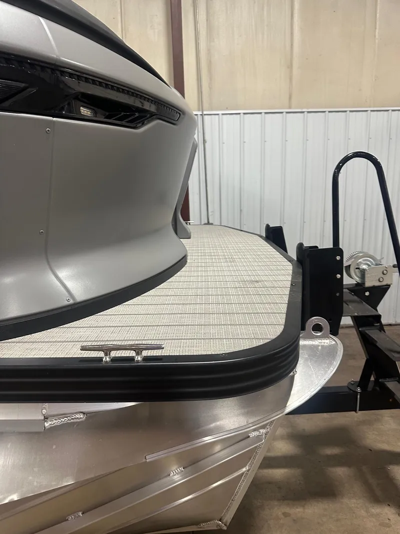 Slide: The Image of 2023 Manitou Explore 24 Navigator boat with trifold bench, close-up view in a warehouse. - 12