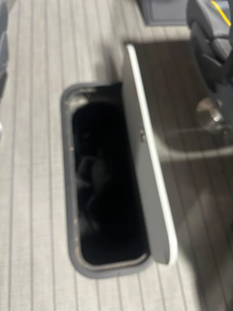 Slide: The Image of Open storage compartment on 2023 Manitou Explore 24 Navigator boat with trifold bench. - 7