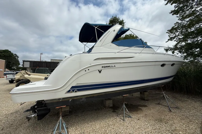 Slide: The Image of 2003 Formula 37 PC boat on stands, white with blue accents, parked outdoors. - 2