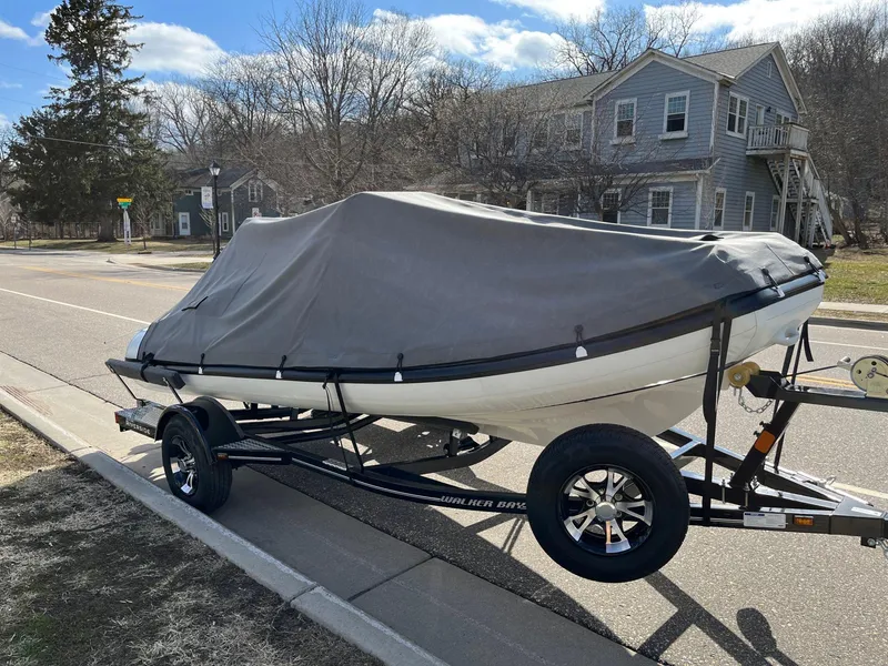 Slide: The Image of 2022 Walker Bay Venture 14 boat covered on a trailer, parked on a suburban street. - 17