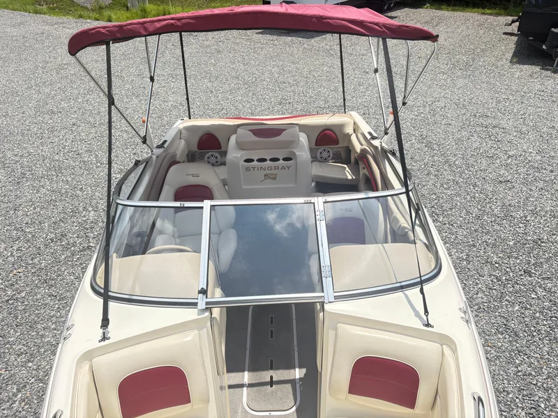 Slide: The Image of 1999 Stingray 190 LS boat with red canopy and seating, parked on gravel. - 11