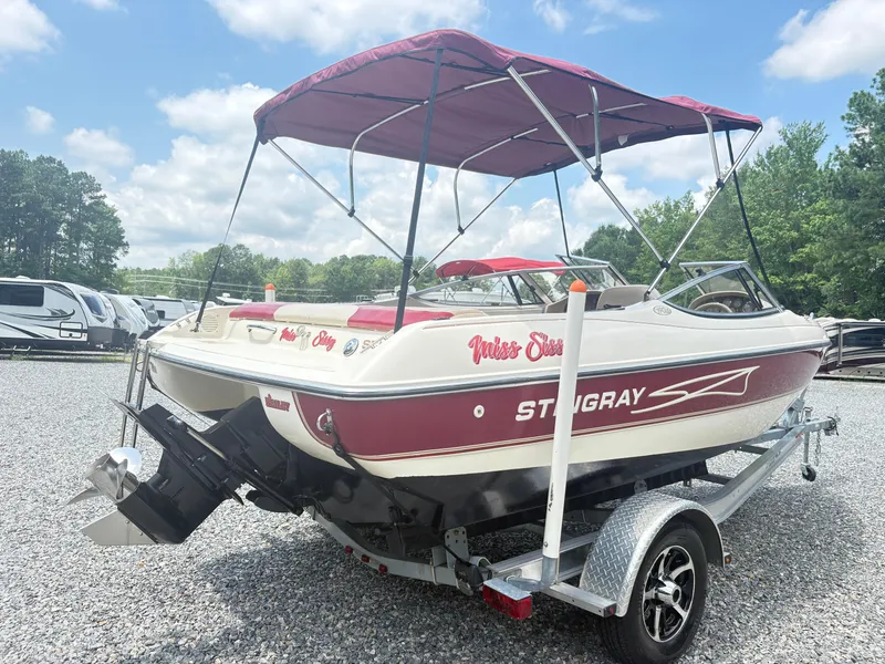 Slide: The Image of 1999 Stingray 190 LS boat with red canopy on a trailer, parked outdoors. - 4