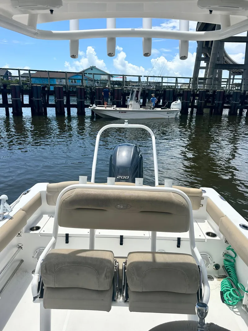 Slide: The Image of 2016 Sea Hunt Ultra 225 boat on water, view from rear, with dock and another boat nearby. - 9
