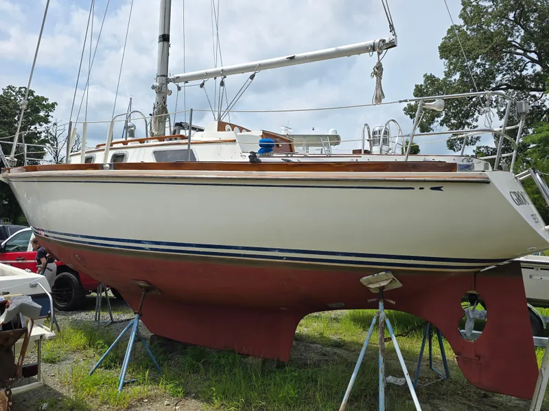 Slide: The Image of 1984 Bristol 31.1 sailboat on land, white hull, red bottom, surrounded by trees and equipment. - 2