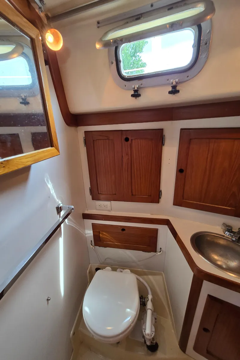 Slide: The Image of 1984 Bristol 31.1 yacht bathroom with wooden cabinets, porthole, and compact toilet. - 28