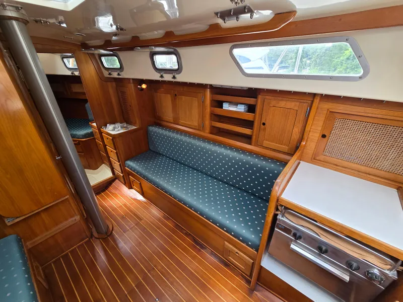 Slide: The Image of 1984 Bristol 31.1 yacht interior with wood finish, blue cushioned seating, and compact kitchen area. - 4