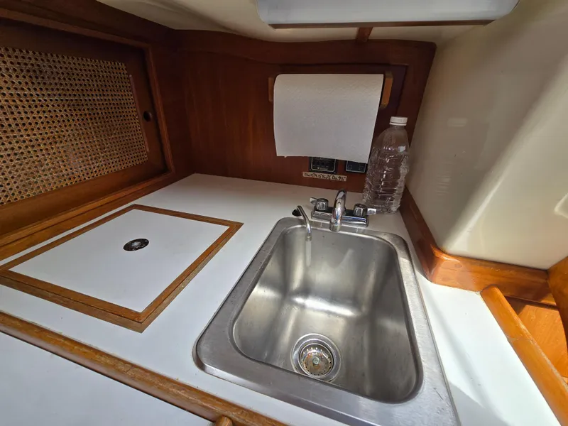 Slide: The Image of Compact kitchen sink area in a 1984 Bristol 31.1 boat, featuring wood accents and a paper towel holder. - 5