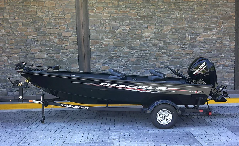 The Image of 2025 Tracker Super Guide V-16 T boat on trailer, parked against stone wall. - 0