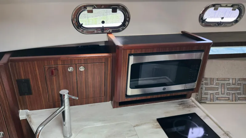 Slide: The Image of 2023 Pursuit OS 325 Offshore kitchen with microwave, sink, and wooden cabinetry. - 24