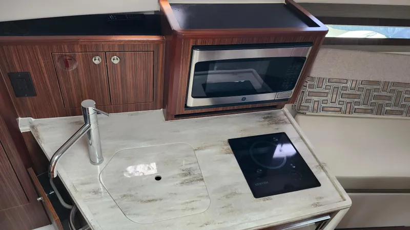 Slide: The Image of 2023 Pursuit OS 325 Offshore boat kitchen with sink, microwave, and cooktop. - 25