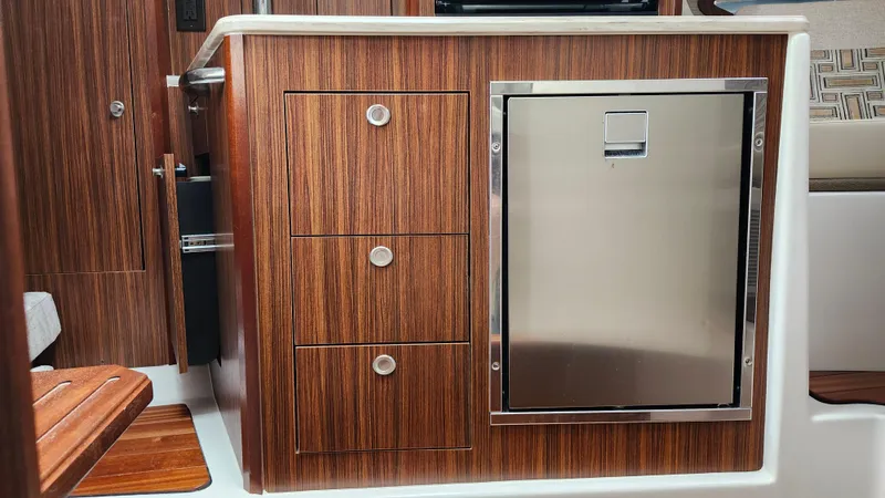 Slide: The Image of 2023 Pursuit OS 325 Offshore interior with wood cabinetry and stainless steel fridge. - 26