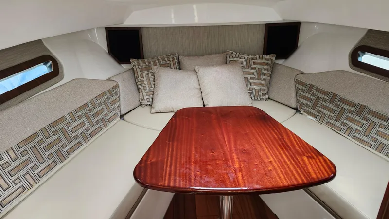 Slide: The Image of 2023 Pursuit OS 325 Offshore cabin with cushioned seating and wooden table. - 28