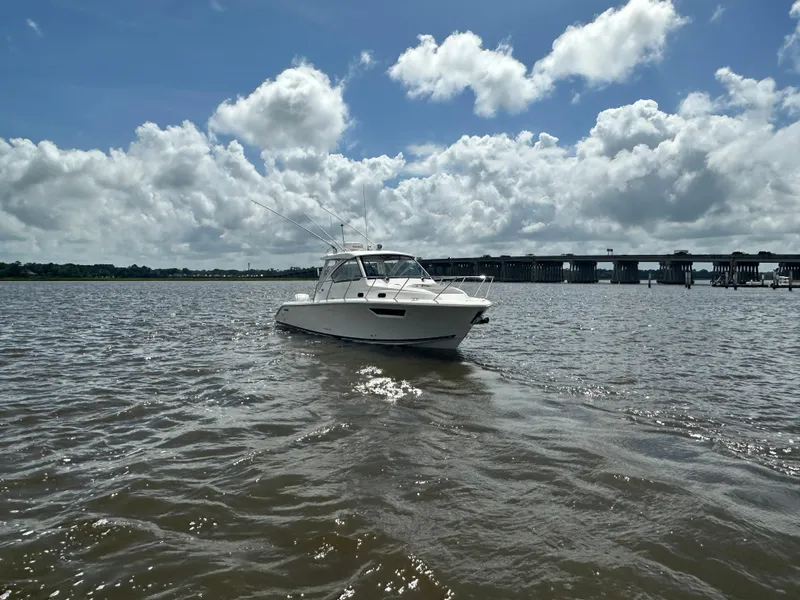 Slide: The Image of 2023 Pursuit OS 325 Offshore boat on water under cloudy sky near a bridge. - 6
