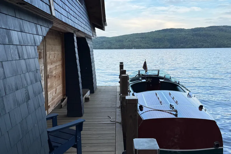 Slide: The Image of 1997 Hacker-Craft 26' Runabout docked by a lakeside cabin with scenic mountain views. - 5