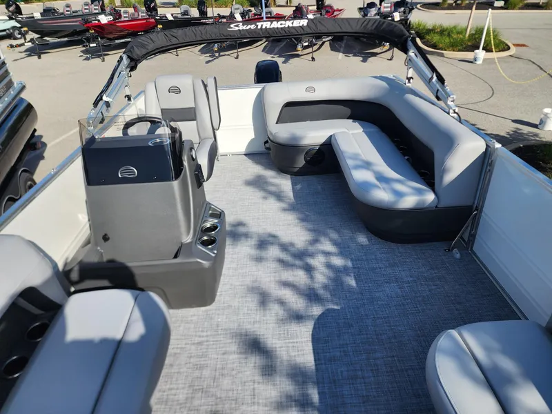 Slide: The Image of 2026 Sun Tracker Party Barge 16 interior with gray seating and helm, parked outdoors. - 4