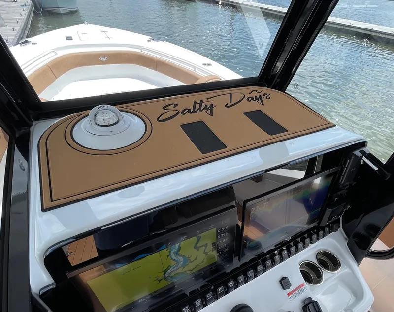 Slide: The Image of 2024 Sea Hunt Ultra 305 SE boat dashboard with navigation screens and compass, docked by the water. - 31
