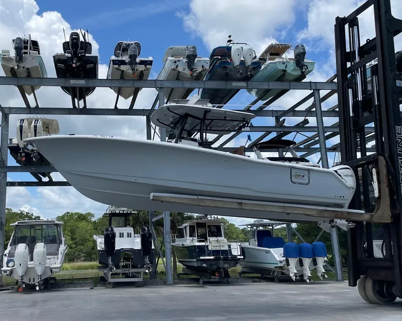 Slide: The Image of 2024 Sea Hunt Ultra 305 SE boat on forklift, surrounded by stacked boats under a blue sky. - 5
