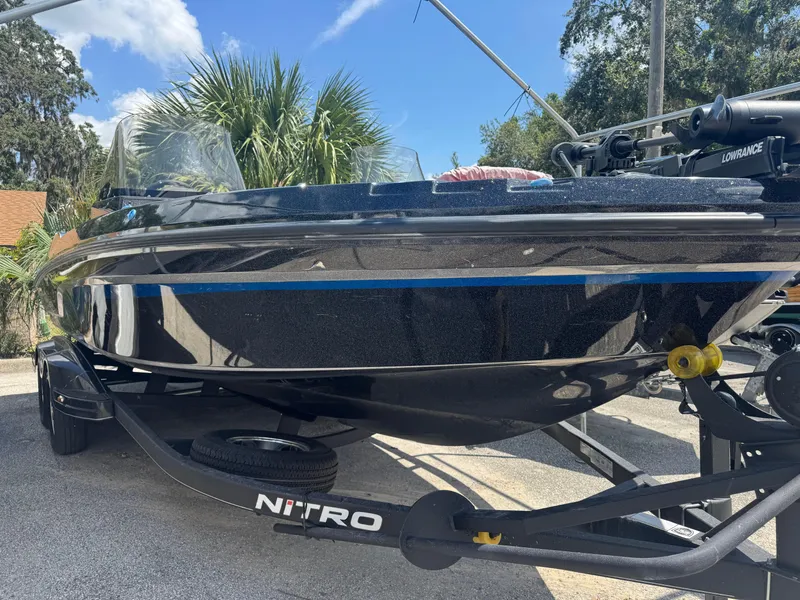 The Image of 2024 Nitro ZV21 boat on trailer, sleek black design with blue accents, parked outdoors. - 0