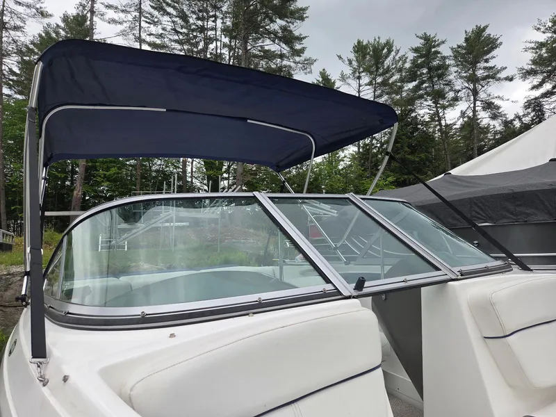 Slide: The Image of 2013 Rinker 186 Captiva boat with blue canopy and windshield, surrounded by trees. - 5