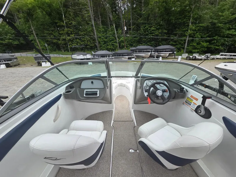 Slide: The Image of 2013 Rinker 186 Captiva boat interior with white seats and steering wheel, surrounded by trees. - 7