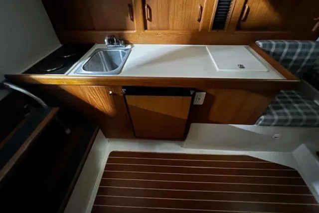 Slide: The Image of 1999 Mainship Pilot 30 Softtop Cruiser interior with kitchenette, sink, and wooden cabinetry. - 4
